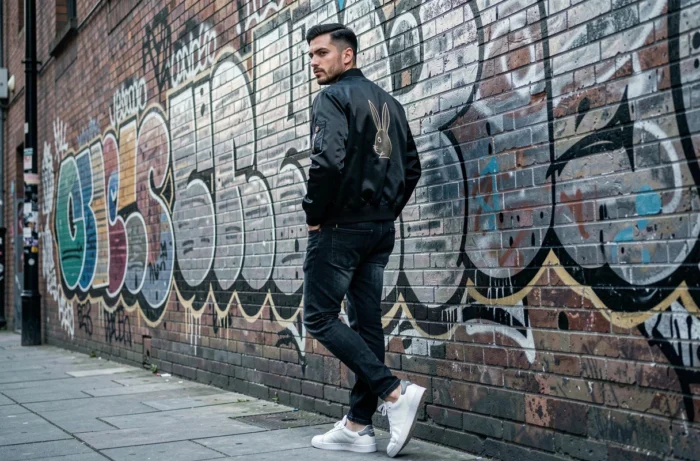 Homme en blouson bomber satiné noir avec motif Playboy dans un décor urbain tendance streetwear